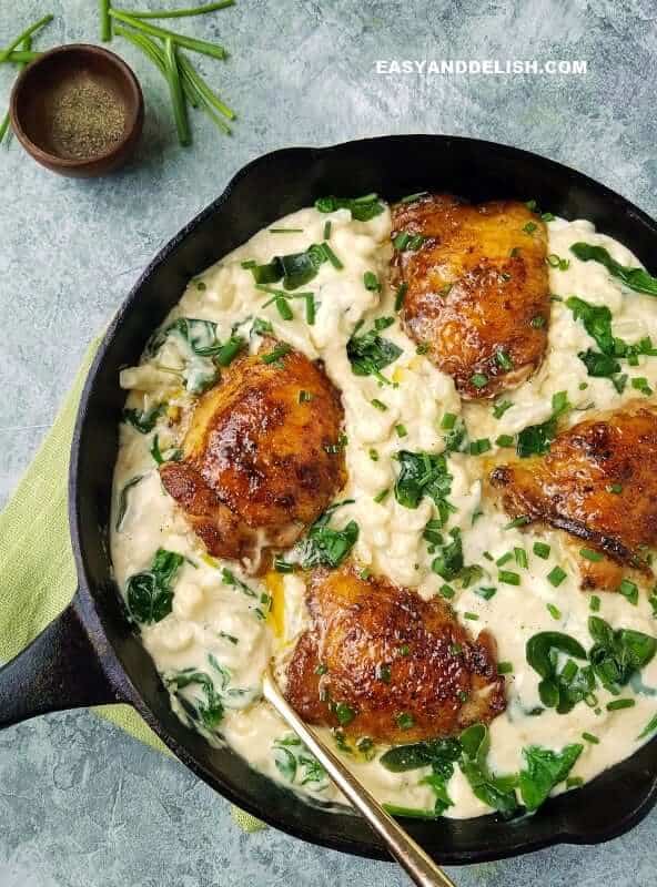 a skillet of cauliflower mac and cheese with chicken thighs and ground pepper on the side