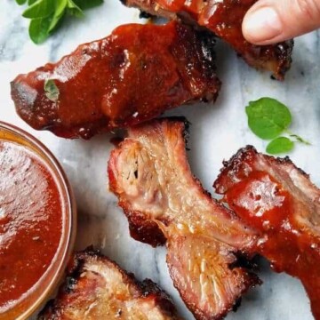 a hand picking a rib of chipotle barbecue pork with other ribs on the side