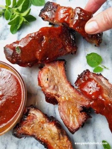 a hand picking a rib of chipotle barbecue pork with other ribs on the side