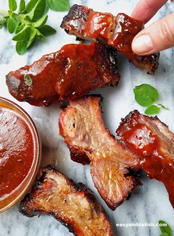a hand picking a rib of grilled baby back ribs with chipotle bbq sauce with other ribs on the side