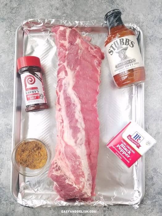 pork rib stack in a baking pan with seasonings and sauce on the side