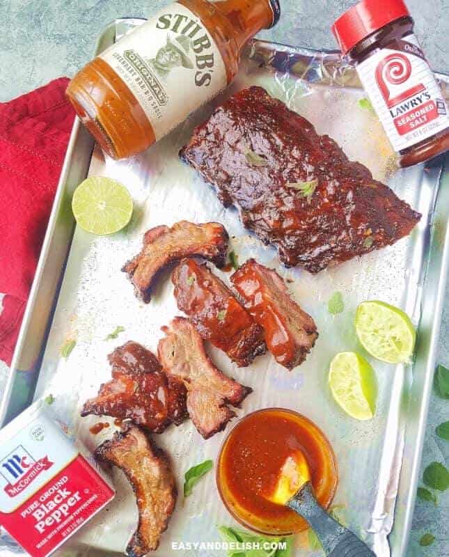 grilled baby back ribs in a sheet pan with sauce, lime and herbs on the side