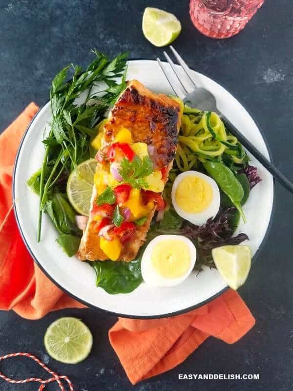 a plate with cooked fish, greens, boiled eggs, and lime