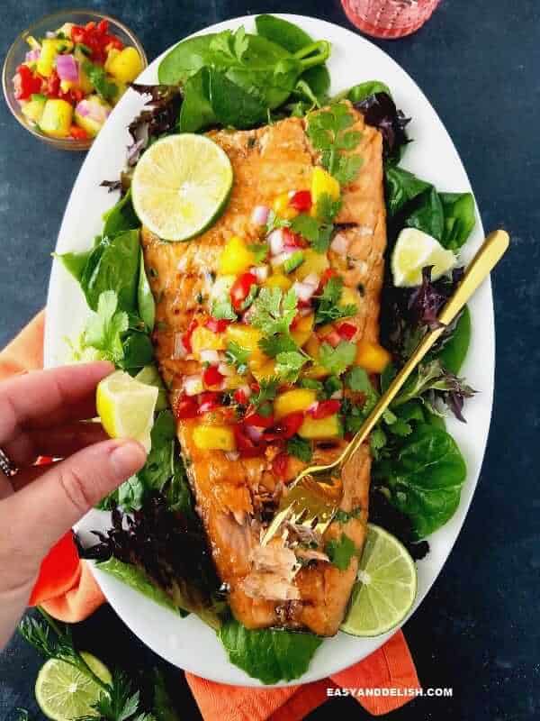 cooked fish in a platter with salsa and lemon wedges