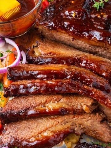 Sliced BBQ beef brisket with vegetables and a bowl of sauce.