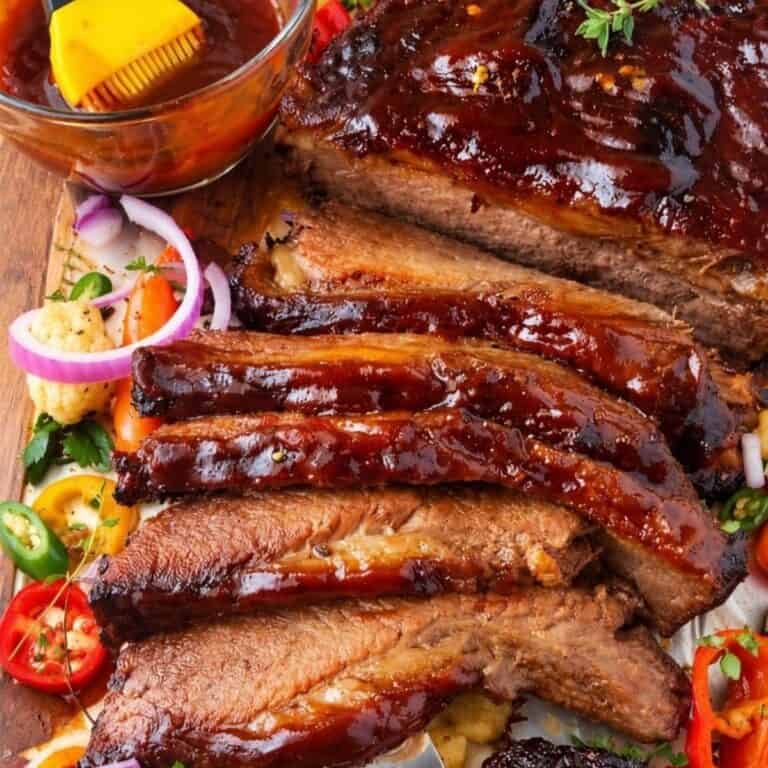 Sliced BBQ beef brisket with vegetables and a bowl of sauce.