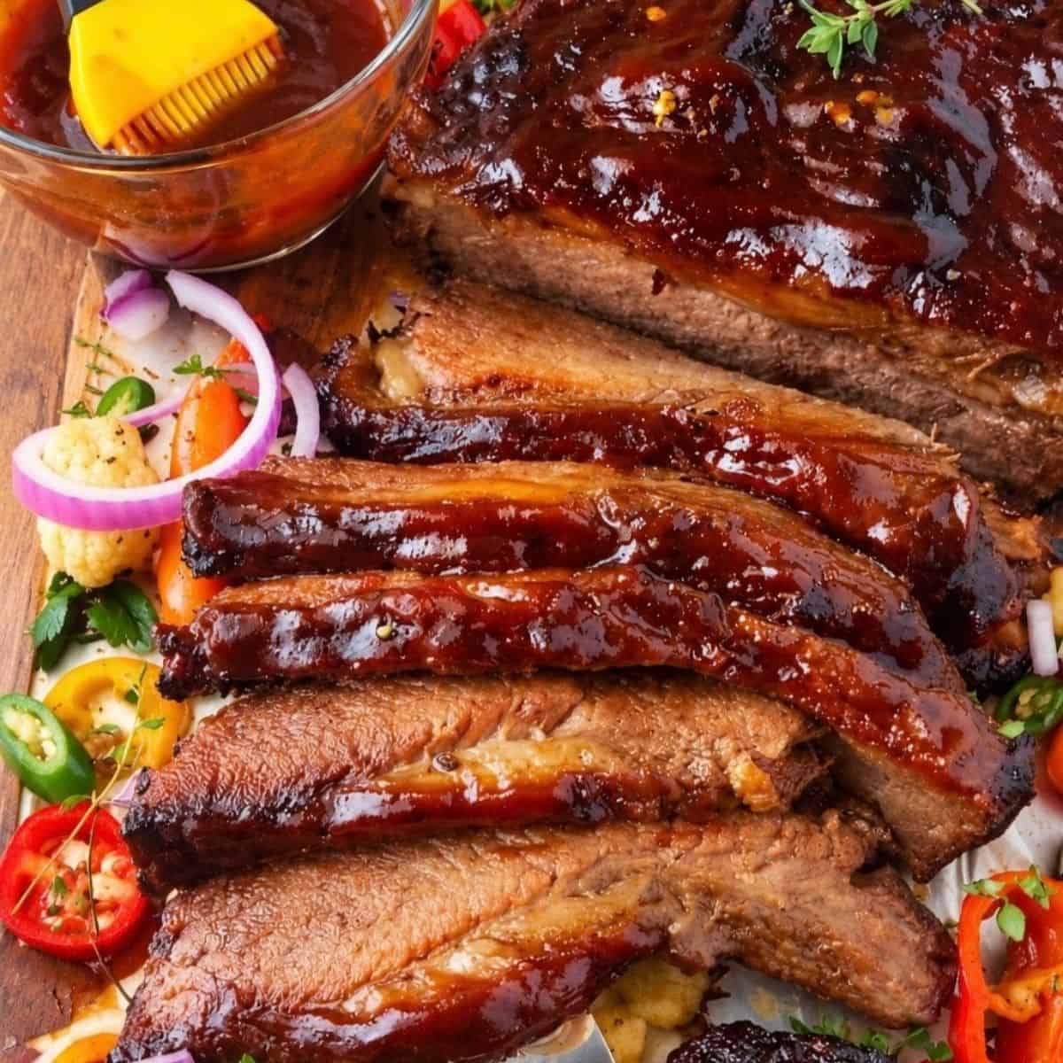 Sliced BBQ beef brisket with vegetables and a bowl of sauce.
