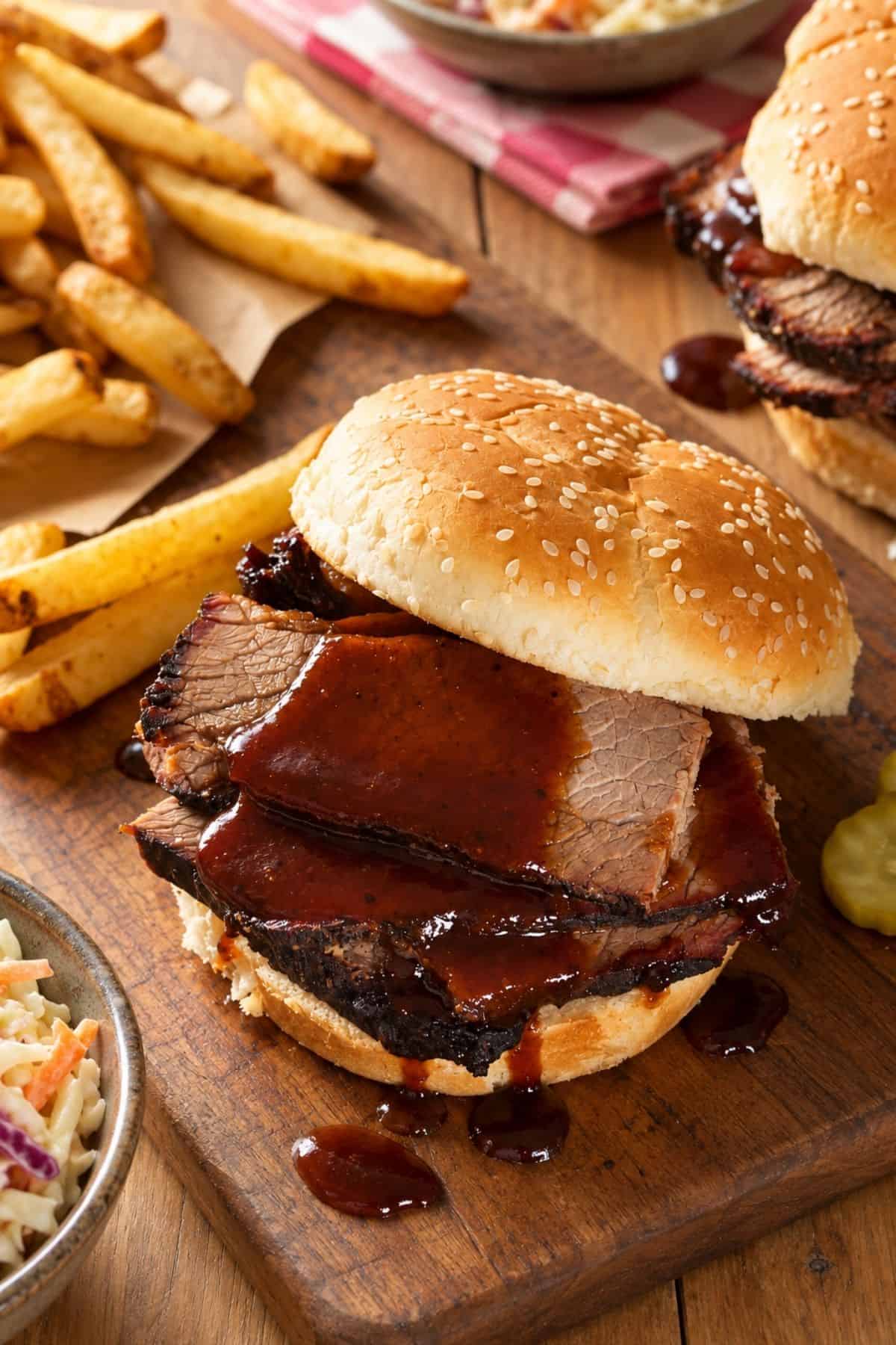Thick slices of saucy beef brisket in a sesame seed bun with French fries on the side.