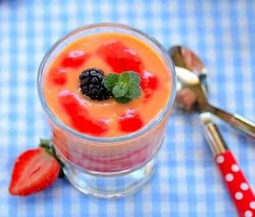 Reddish-orange papaya cream in a dessert glass on a blue checkered table, garnished with a blackberry and mint leaf