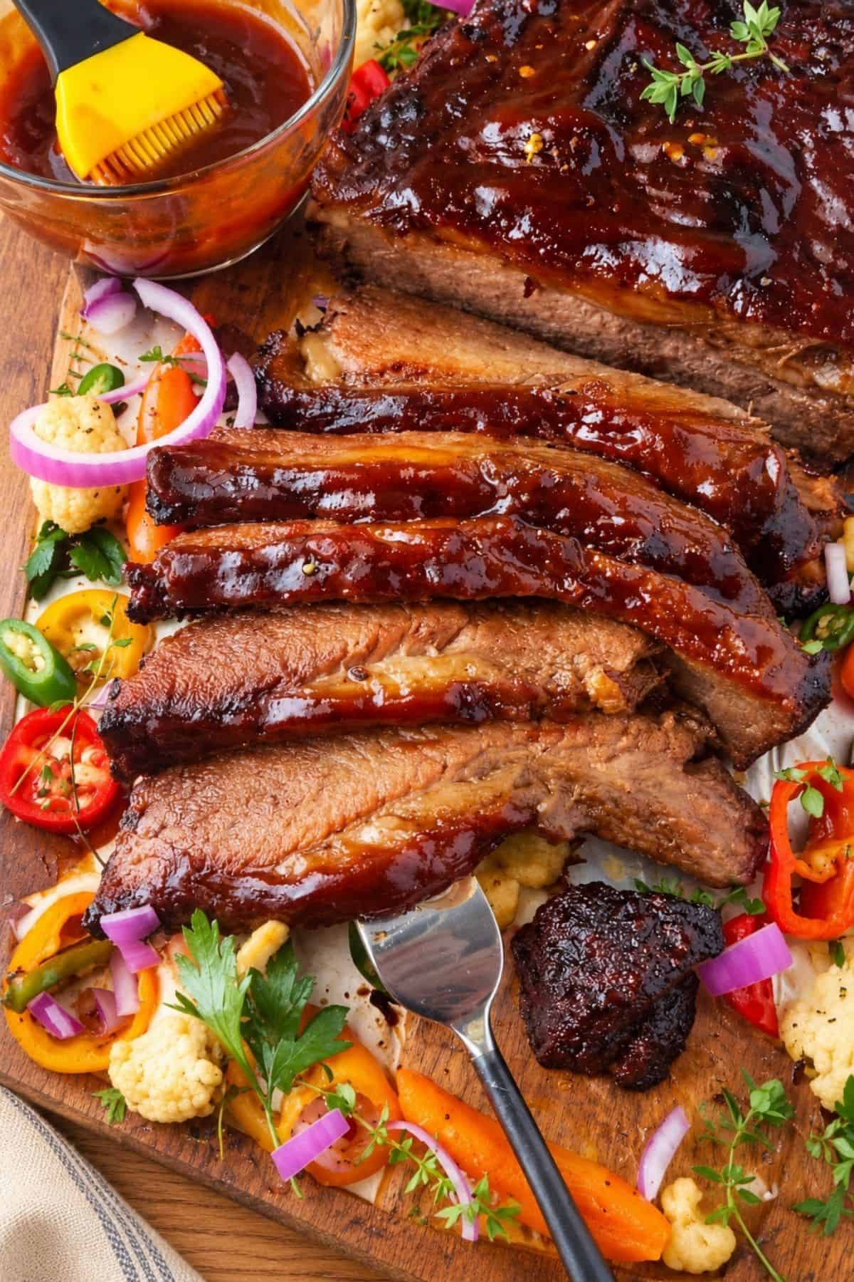 Sliced BBQ beef brisket coated in glossy barbecue sauce with fresh herbs and vegetables.