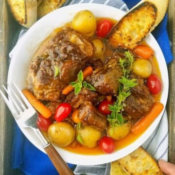A bowl of beef Oxtail with veggies and bread on a tray