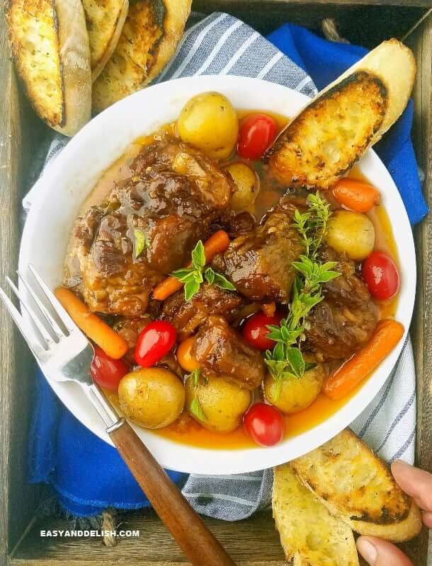 A bowl of beef Oxtail with veggies and bread on a tray