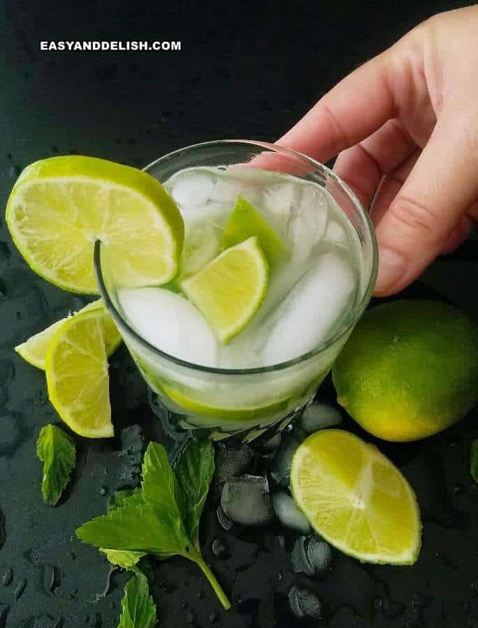 A glass of caipirinha with a hand behind. 