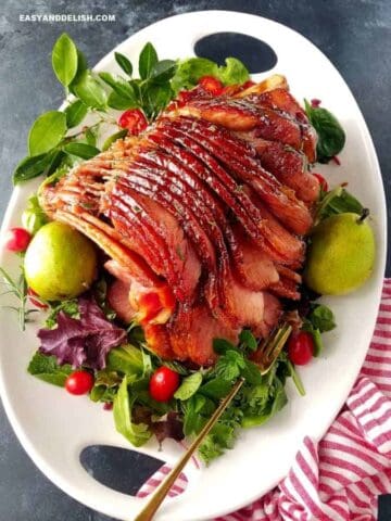 A platter with honey baked ham garnished with pears and veggies