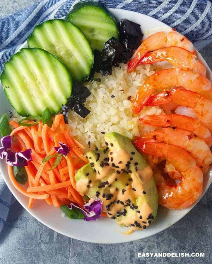 Sushi Bowl Recipe is a trendy low carb sushi made in 15 minutes with seasoned cauliflower rice, cooked shrimp, avocado,veggies, and sriracha mayo. It's low carb, keto, gluten-free. easy and delish! Plus, 10 other sushi recipes for a sushi party. close up image of sushi bowl recipe