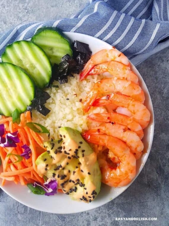 one sushi bowl with cauliflower rice, shrimp, avocado, cucumber, nori, carrots,a nd sriracha mayo. 