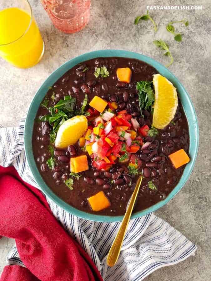 A bowl of vegan Feijoada with garnishes and a glass of juice on the side