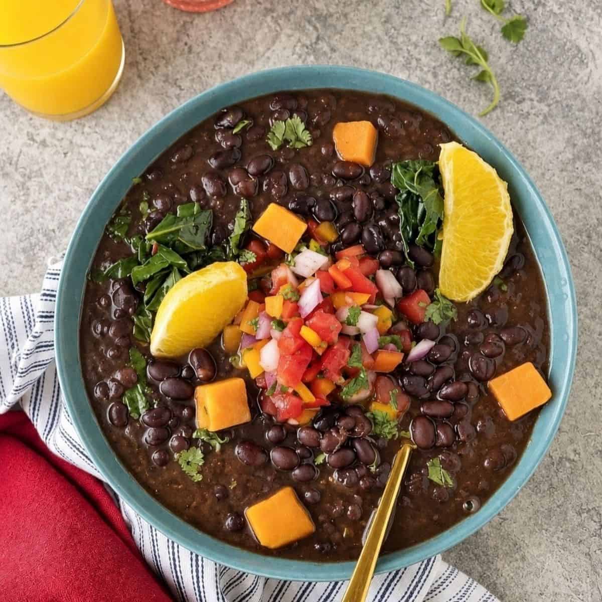 Black bean stew topped with sweet potatoes, fresh salsa, greens, and orange wedges.