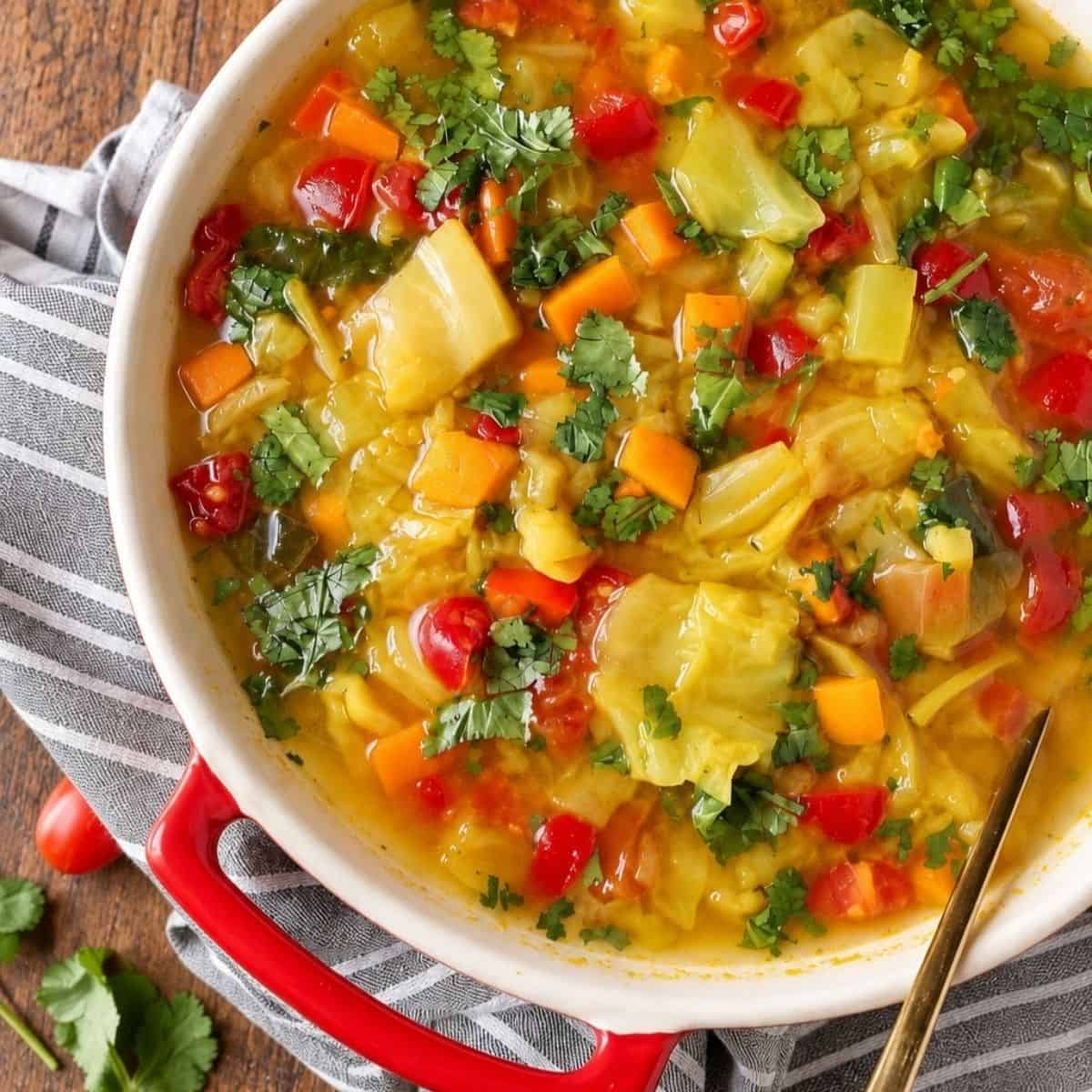 Close-up of cabbage soup with tomatoes, diced vegetables, and chopped herbs in a golden broth.