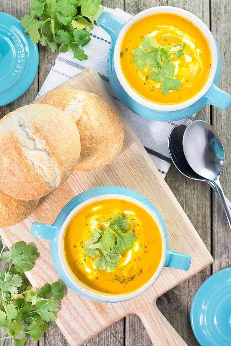 2 bowls of carrot soup with bread on the side