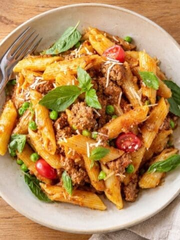 Pasta Bolognese with ground beef, peas, tomatoes, basil, and Parmesan in a bowl.