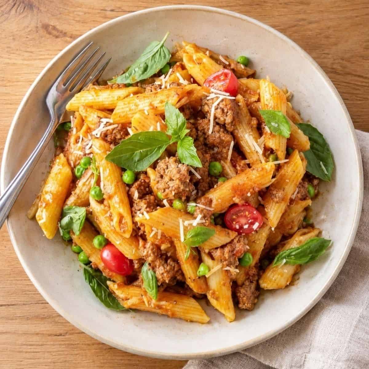 Pasta Bolognese with ground beef, peas, tomatoes, basil, and Parmesan in a bowl.