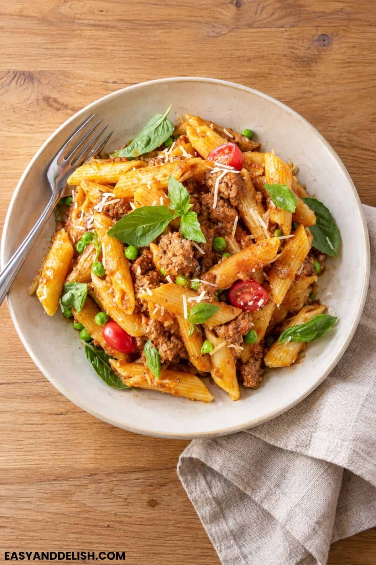 Pasta Bolognese with penne, ground beef, peas, basil, Parmesan, and cherry tomatoes.