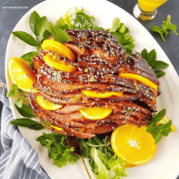 Slow cooker ham with brown sugar glaze and orange slices in a platter.