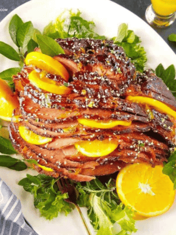 Slow cooker ham with brown sugar glaze and orange slices in a platter.