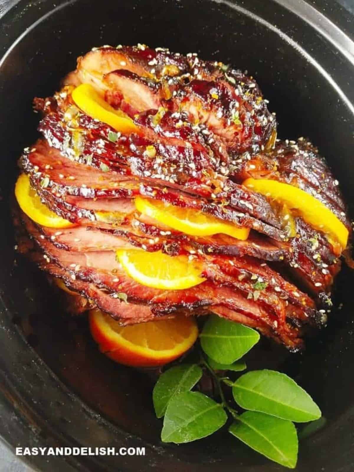 Spiral ham in a slow cooker garnished with orange slices and leaves.