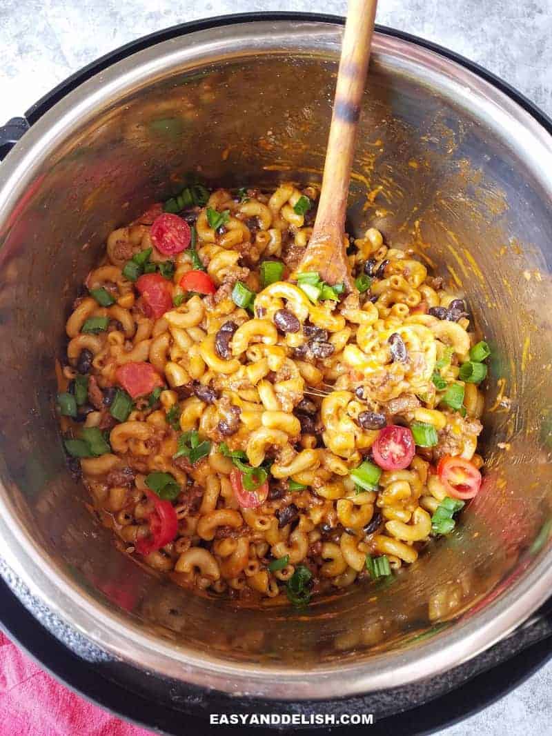 chili mac and cheese in the pressure cooker with a wooden spoon on the side