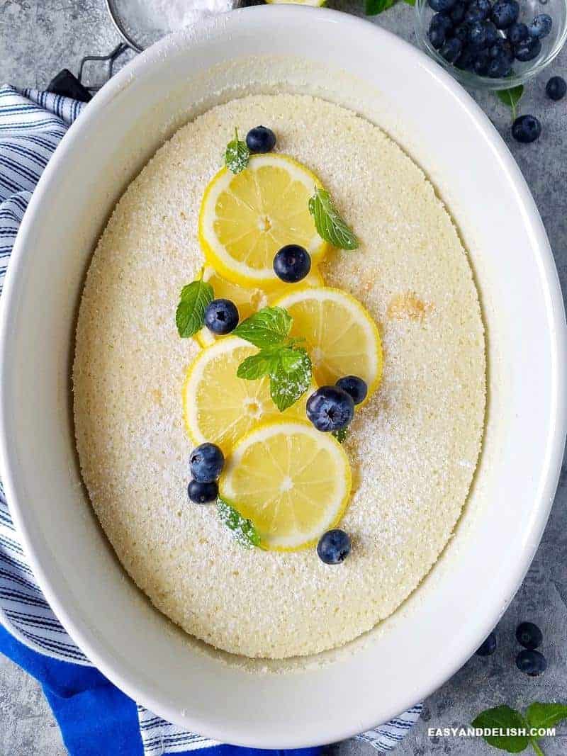 whole lemon pudding cake garnished with lemon slices and blueberries on top