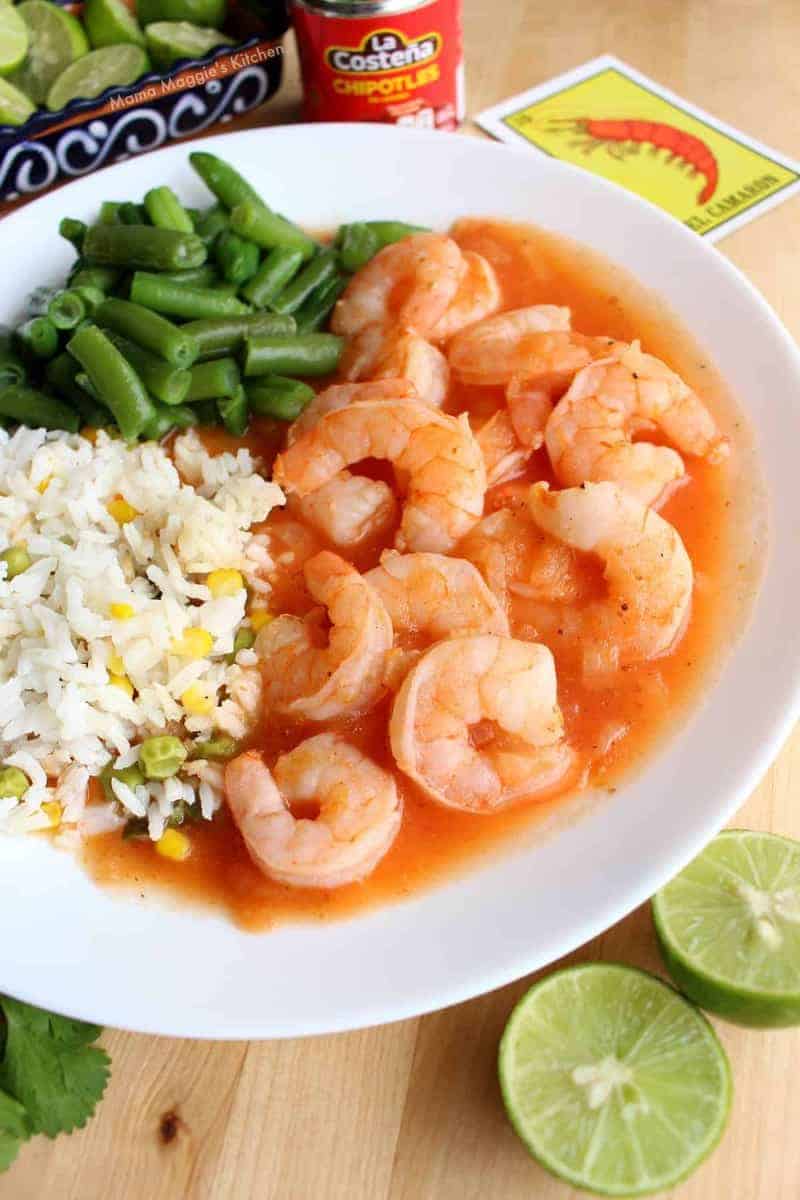 a plate of shrimp, rice and green beans with limes on the side 