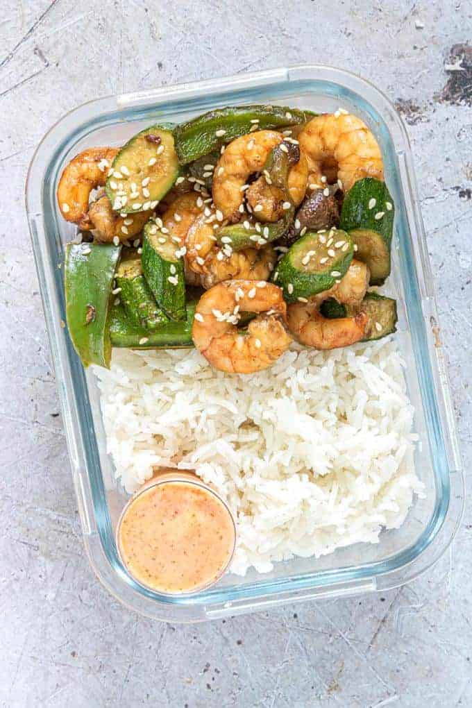 shrimp, vegetables and rice in a container with a bowl of sauce 