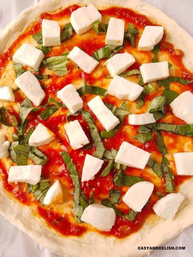 close up showing pizza crust topped with tomato sauce,mozzarella, and basil