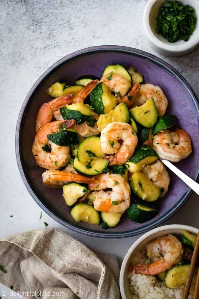 shrimp and zucchini in a bowl with ganishes on the side