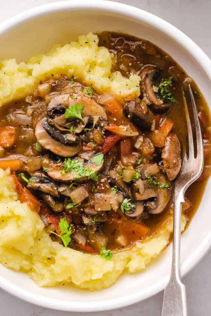 mushroom stew over mashe potatoes in a bowl with fork on the side