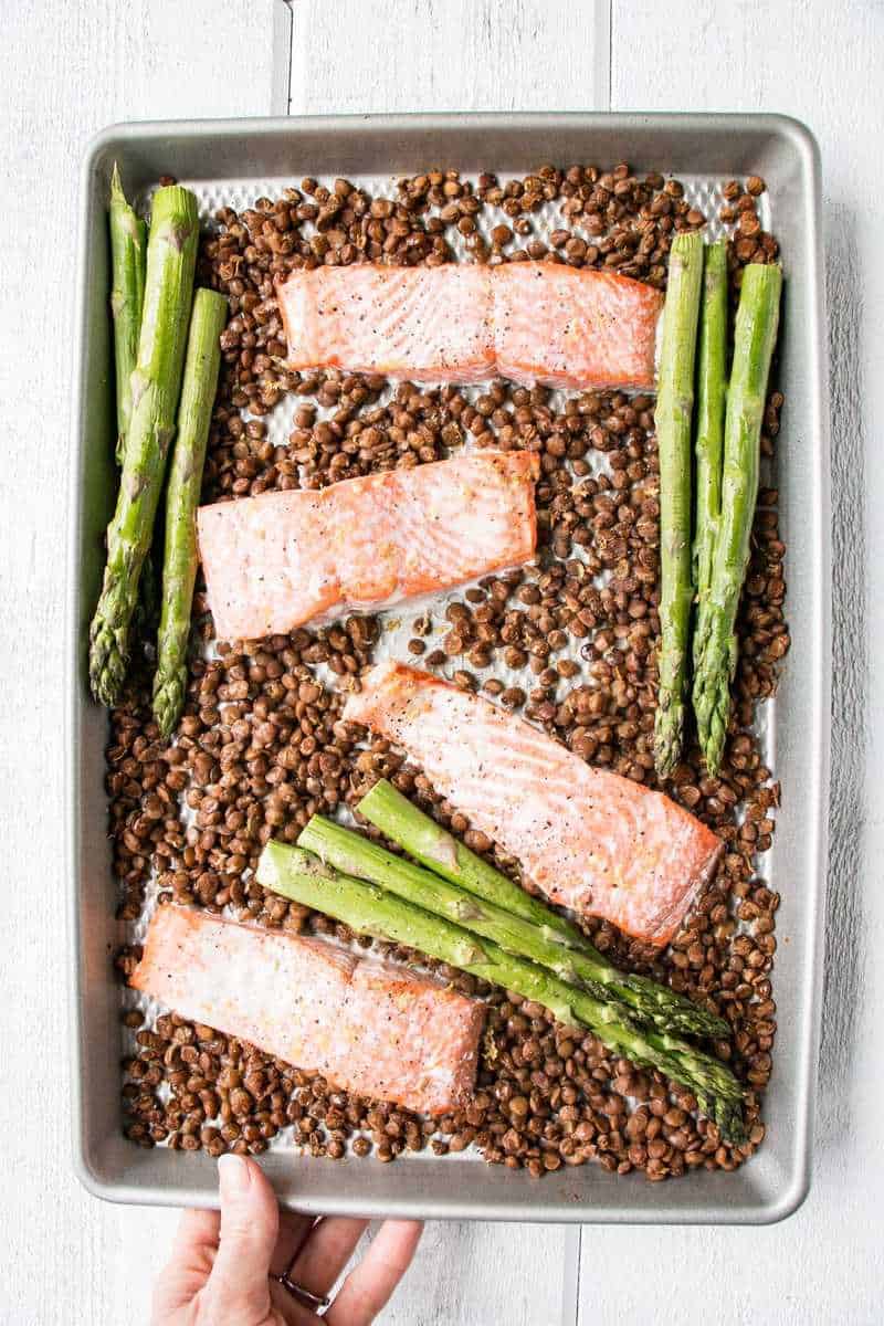 salmon , lentils and asparagus in a sheet pan with a hand holding it