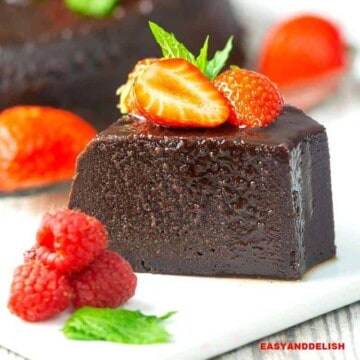 A slice of chocolate bread pudding flan on a plate with berries on top and on the side.