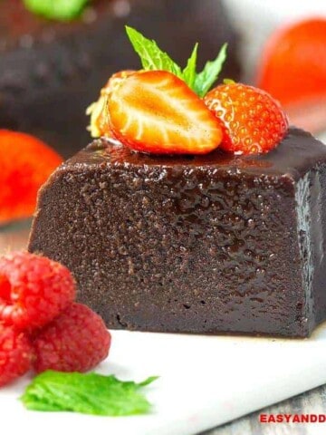 A slice of chocolate bread pudding flan on a plate with berries on top and on the side.