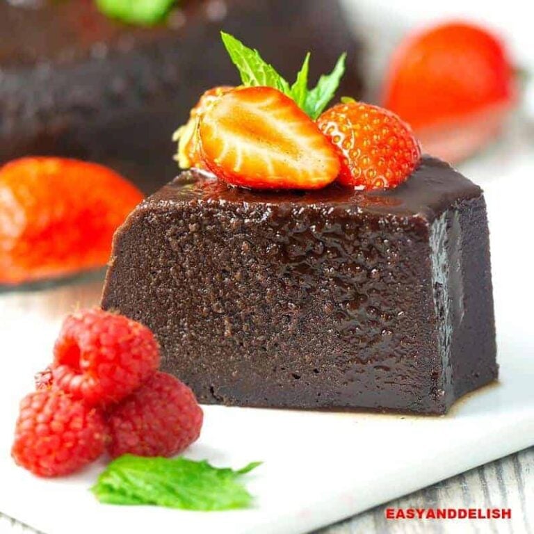 A slice of chocolate bread pudding flan on a plate with berries on top and on the side.
