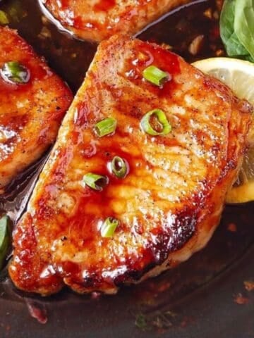 Pan-seared pork chops coated in teriyaki glaze with green onions and lemon slices.