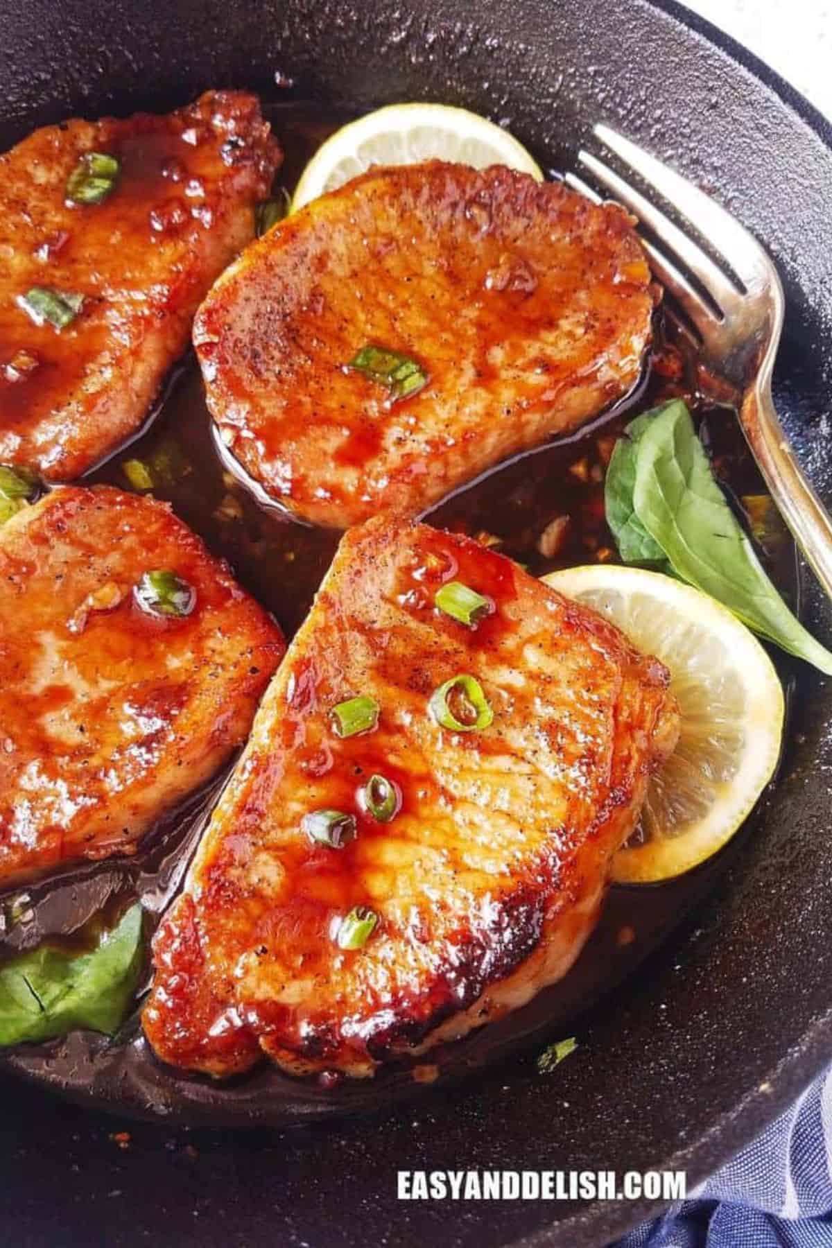 Boneless pork chops with teriyaki sauce, lemon slices, and fresh basil in a cast-iron skillet.