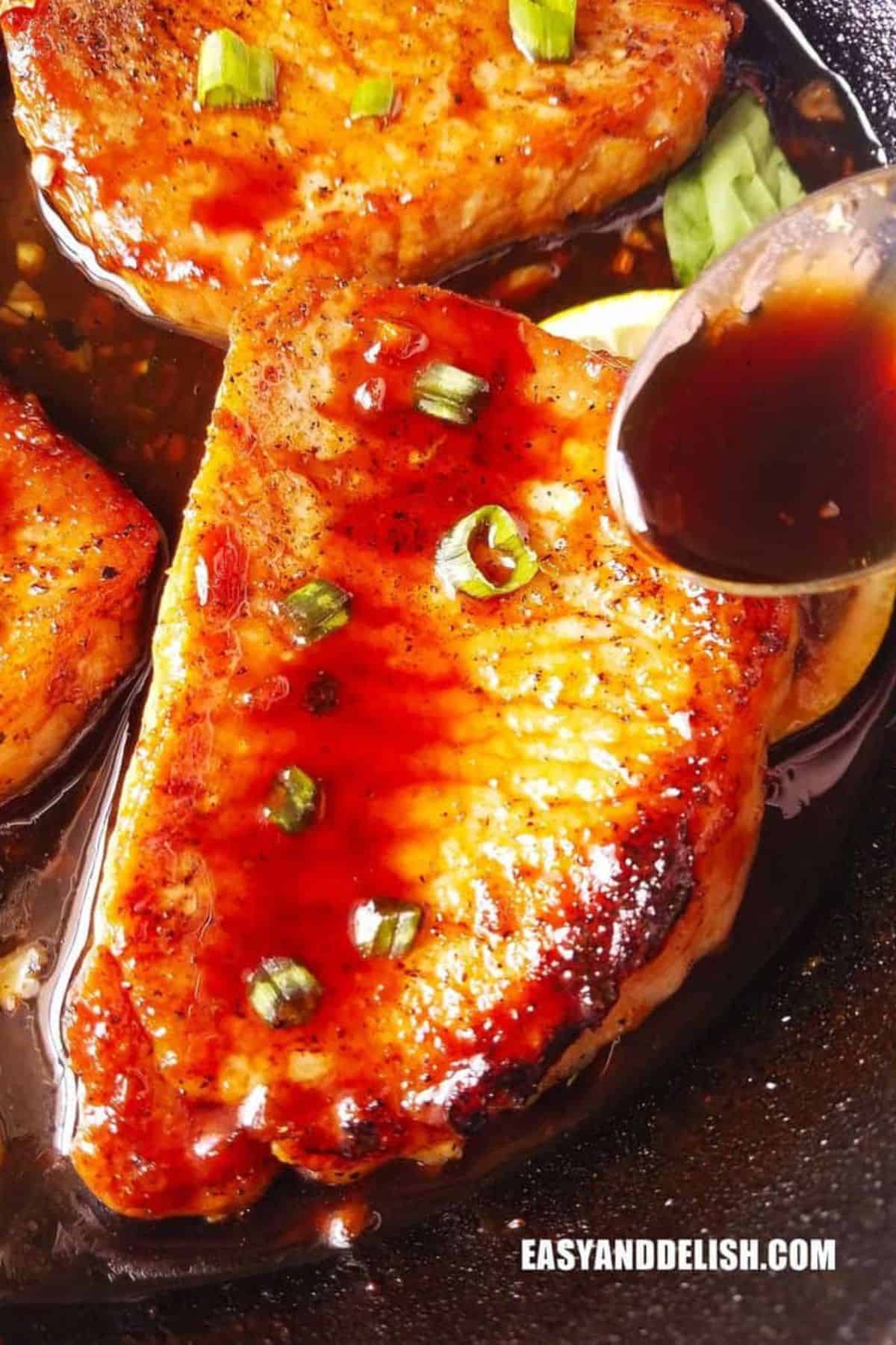 Teriyaki sauce spooned over a golden seared pork chop with green onions.