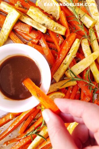roasted carrots and parsnips being dipped in a dressing