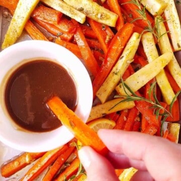 roasted carrots and parsnips being dipped in a dressing