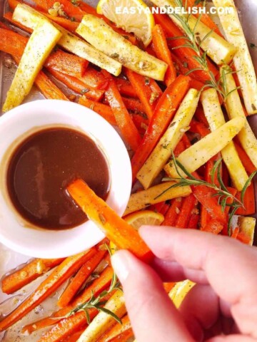 roasted carrots and parsnips being dipped in a dressing