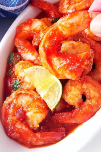 one shrimp a la diabla being held with a hand out of a bowl