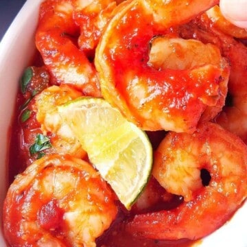 one shrimp a la diabla being held with a hand out of a bowl