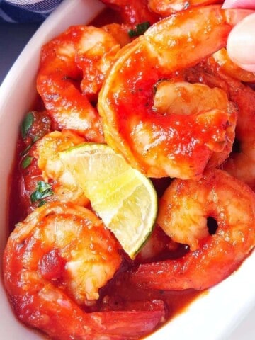 one shrimp a la diabla being held with a hand out of a bowl